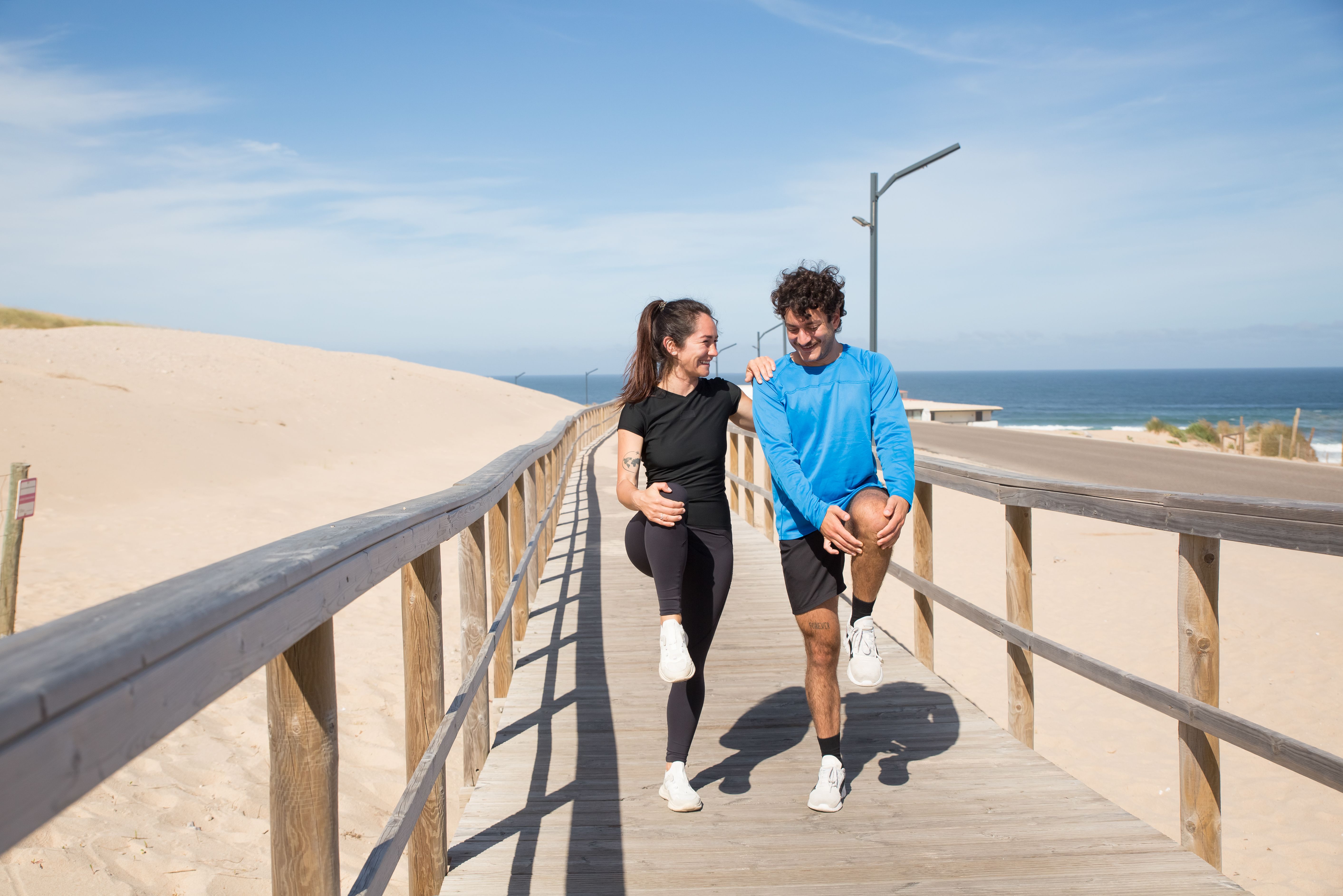 Healthy adult man and woman warming up together on a coastal boardwalk